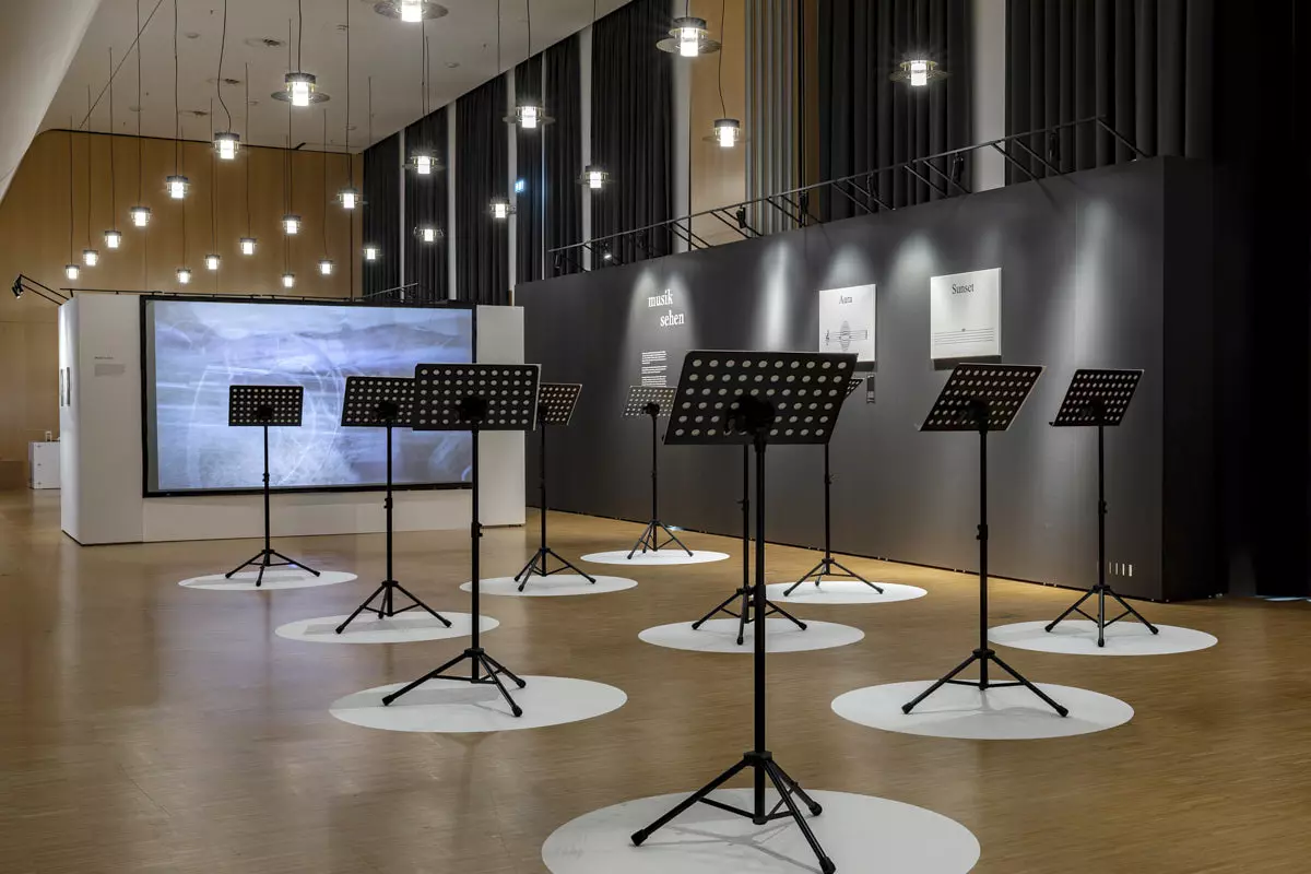 Ausstellung „Musik aufs Auge“ in der Württembergischen Landesbibliothek Stuttgart: Notenständer auf weißen Kreisen vor einer dunklen Mila-wall Wand